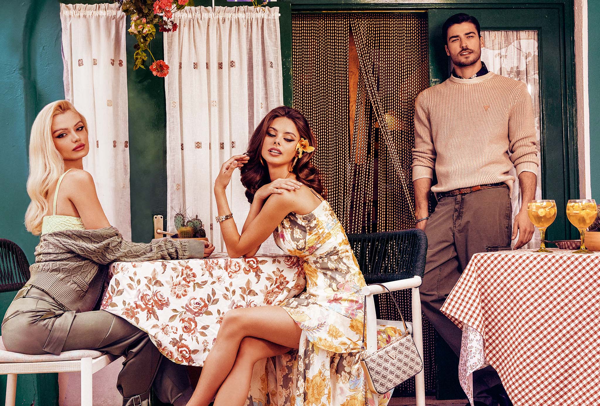 A photo of Guess models sitting at a table on a cafe patio with a man admiring them
